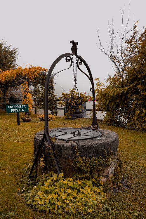 Free Charming stone well in a serene autumn garden with lush foliage. Stock Photo