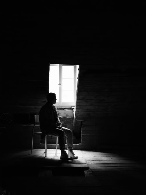 Free Silhouette of a person lost in thought by a window in a dimly lit room. Stock Photo