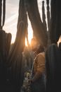 Side view of male farmer standing among tall green cactuses with prickly spikes while working in garden with bright sunbeam