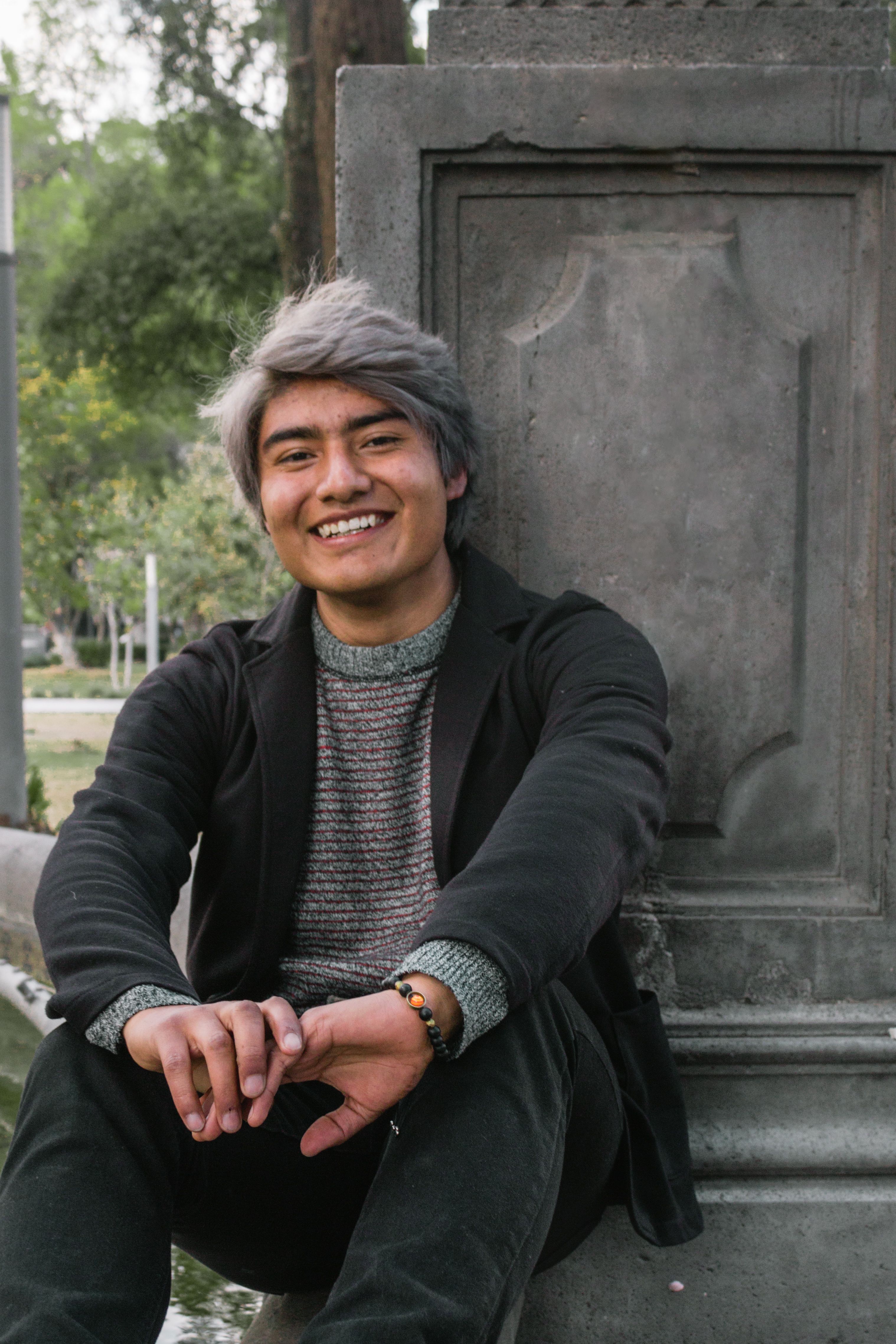 A cheerful young man with gray hair smiling while sitting outdoors in Mexico.