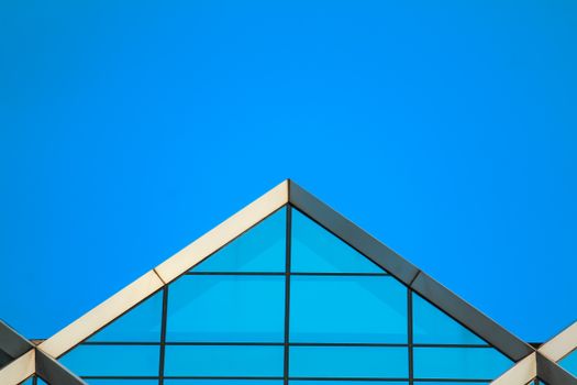 Abstract view of a modern glass building roof against clear blue sky.
