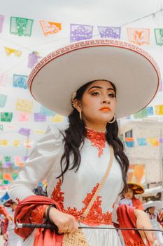 A woman in traditional Mexican attire at a lively cultural festival with colorful papel picado.