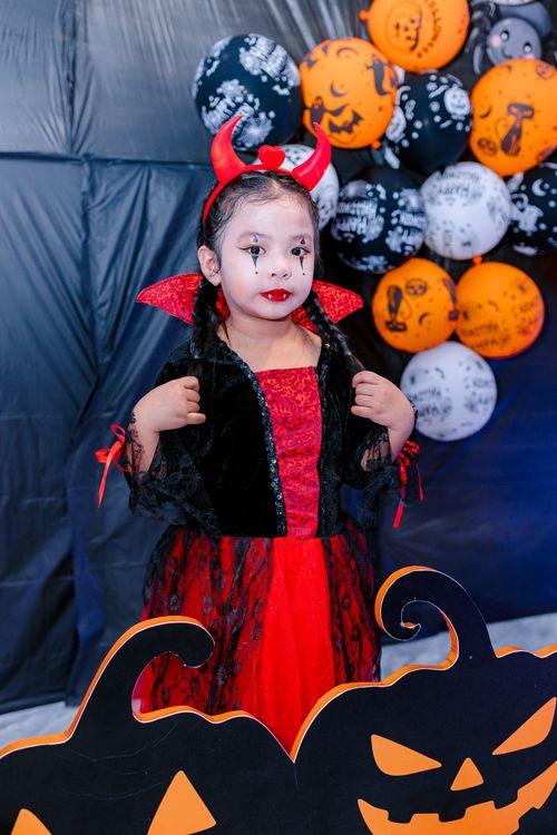 Free Adorable child in a devil costume at a Halloween party with pumpkins and spooky balloons. Stock Photo