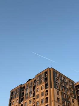 An elegant apartment building in Baku under a clear blue sky with an airplane contrail.
