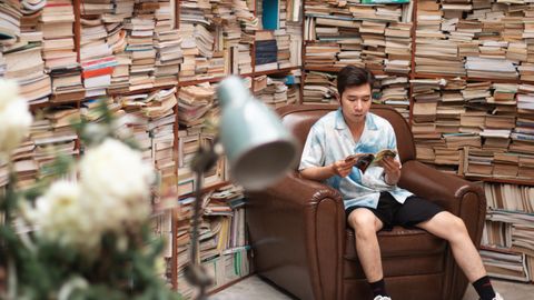 A young man enjoys reading in a leather chair surrounded by books in Ho Chi Minh City.