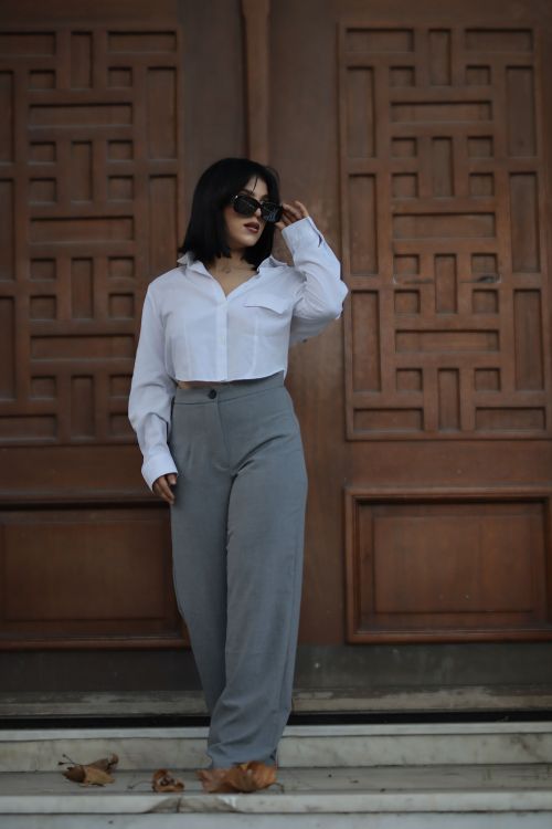 Free Stylish woman in white blouse and grey trousers standing confidently outdoors. Stock Photo