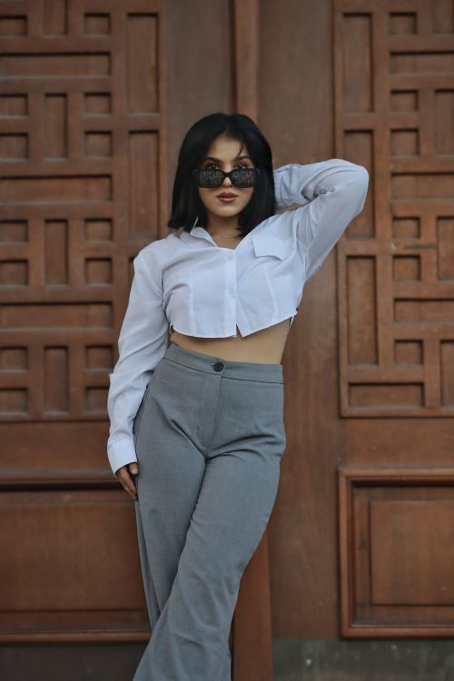 Free Confident woman in chic outfit poses against a wooden backdrop, showcasing modern fashion. Stock Photo