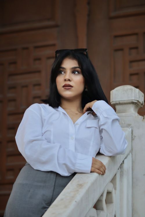 Free Elegant woman with long black hair and white blouse leaning on a railing outdoors. Stock Photo