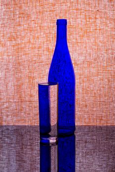 Artistic composition featuring a blue glass bottle and tumbler with a patterned backdrop.