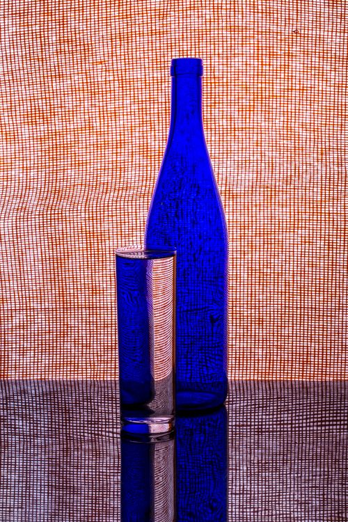Free Artistic composition featuring a blue glass bottle and tumbler with a patterned backdrop. Stock Photo