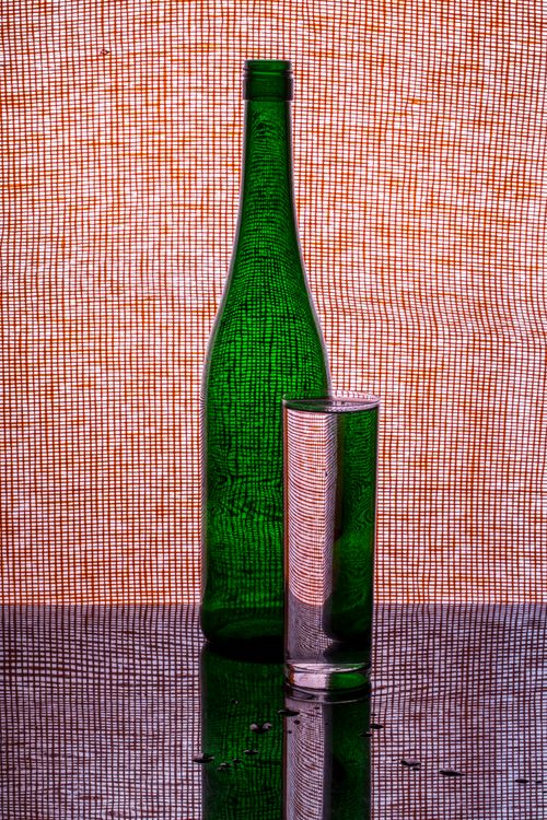 Free Artistic still life featuring a green bottle and glass against a textured background. Stock Photo