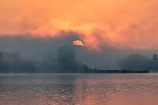 A calm sunrise with mist over a peaceful lake creating a tranquil atmosphere.