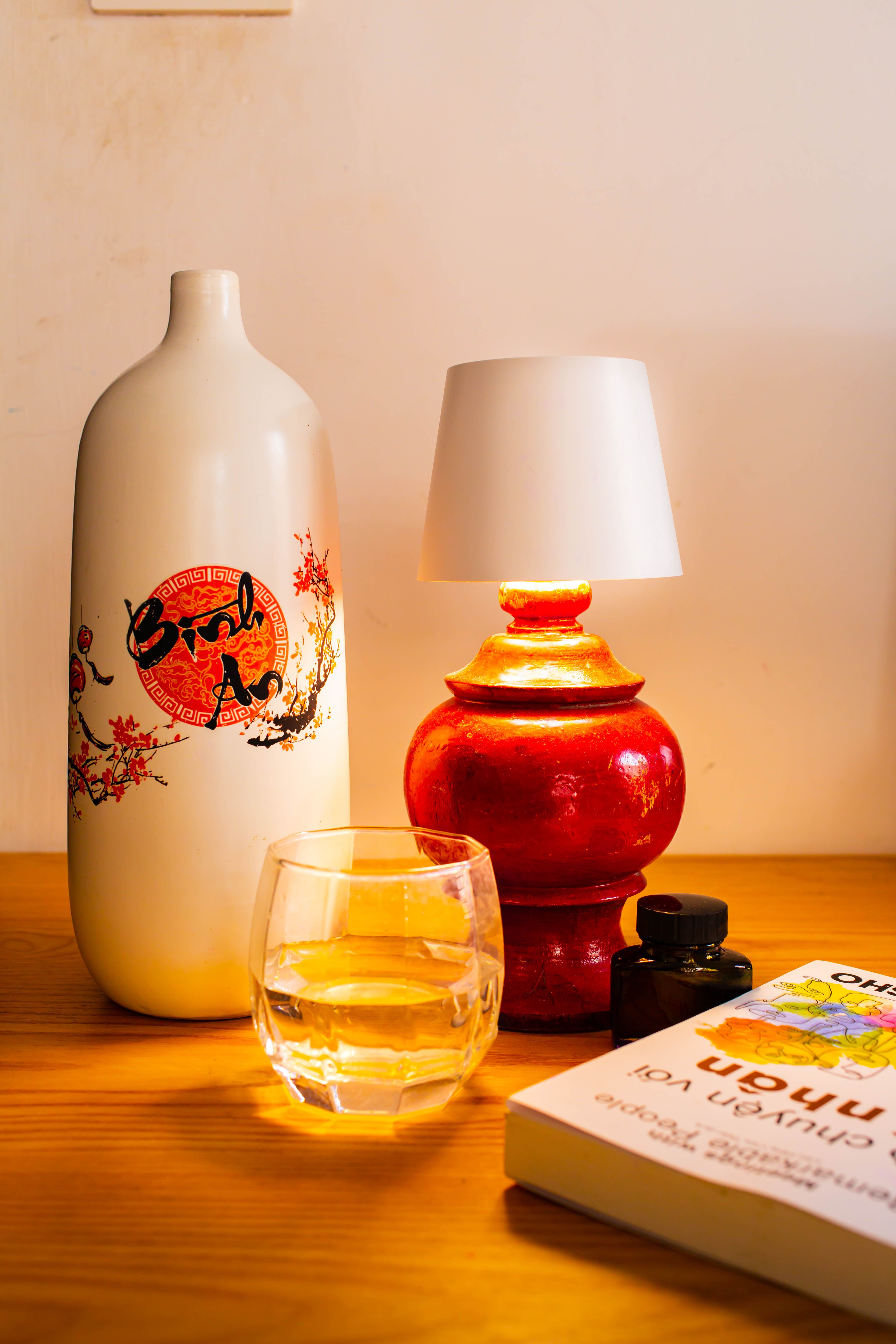 Warm still life featuring a lamp, whiskey, and art items on a wooden table.