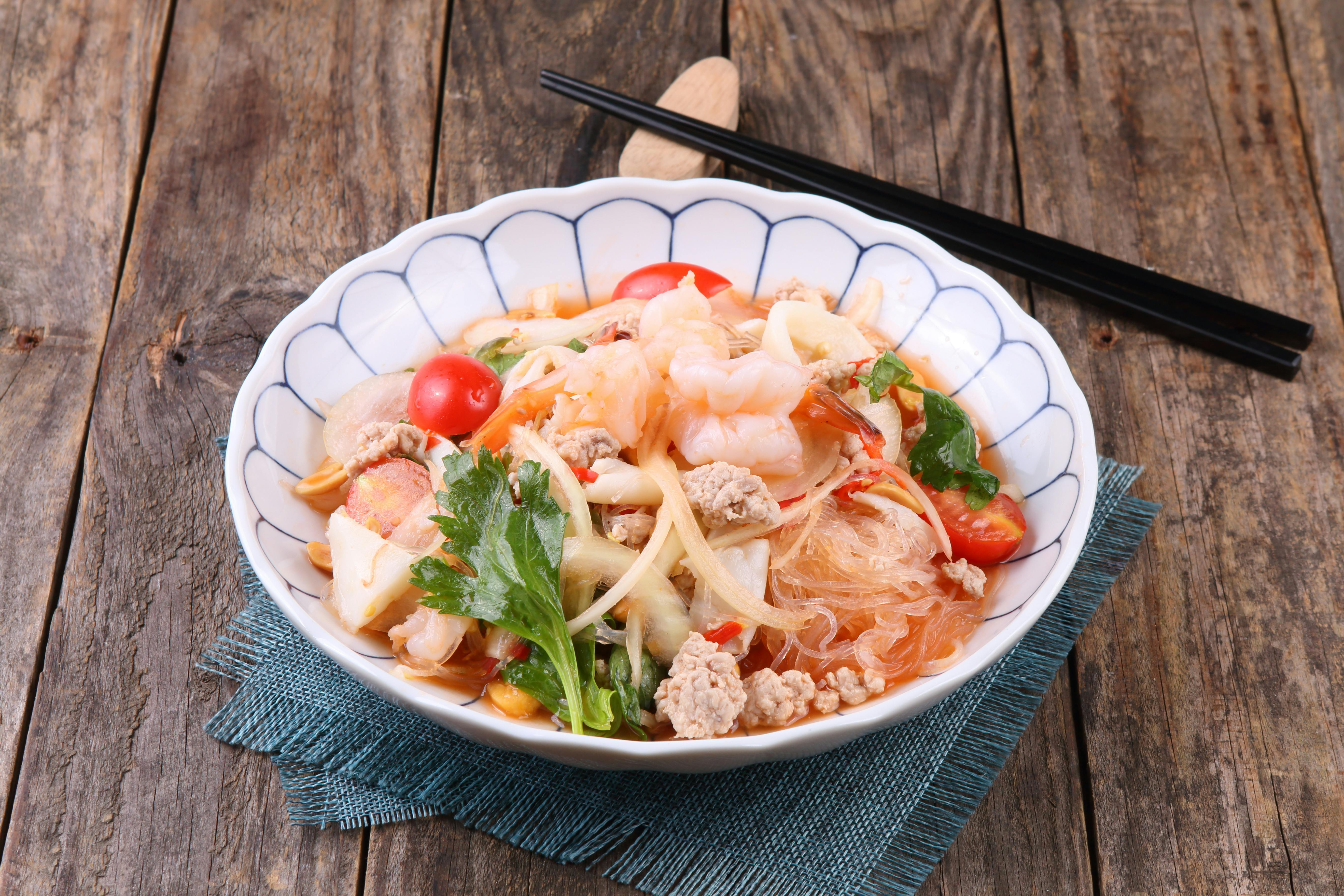 Flavorful Thai glass noodle salad with shrimp, minced pork, and fresh vegetables in a white bowl.