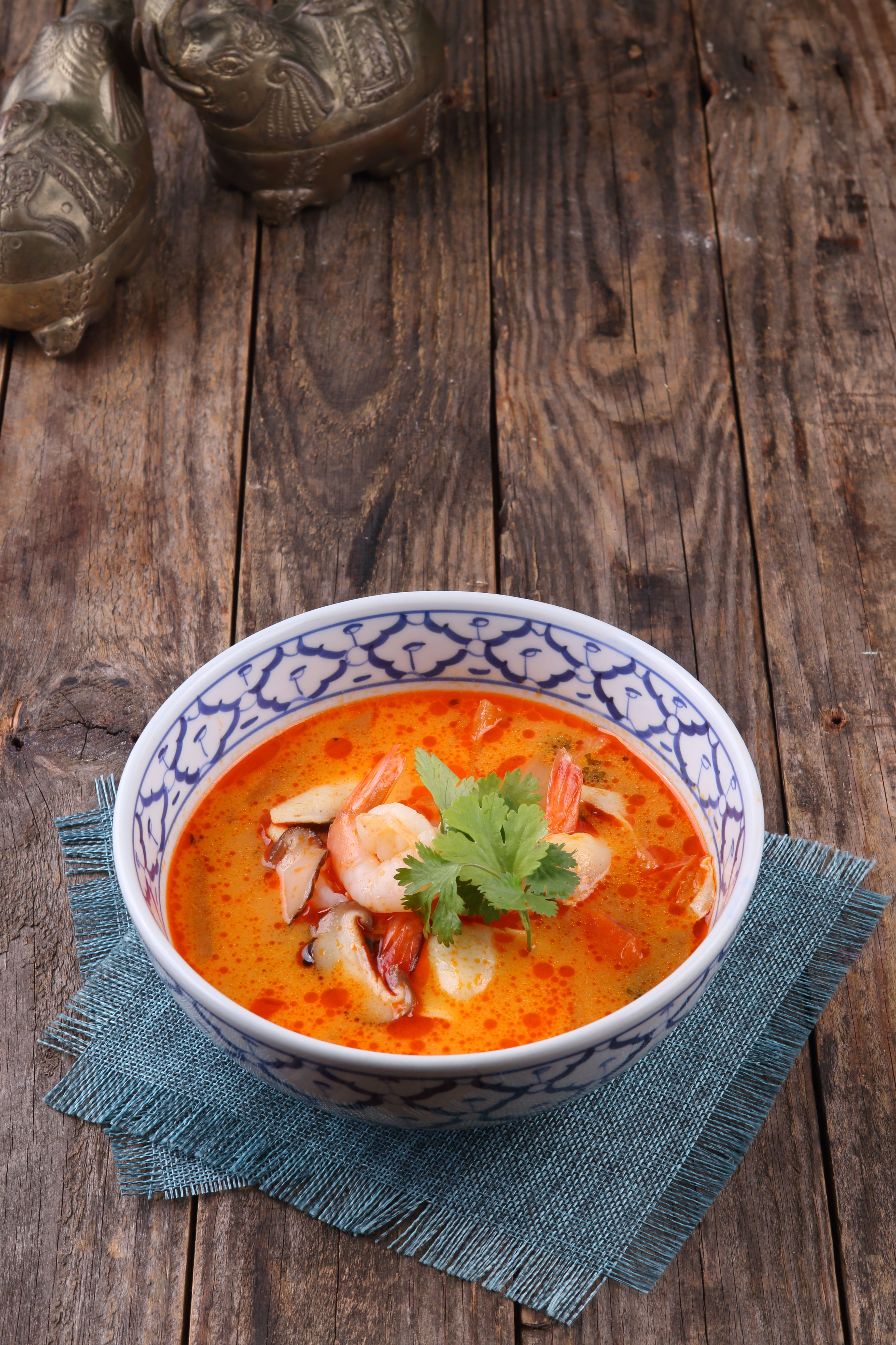 Delicious bowl of traditional Thai Tom Yum soup with shrimp, served in a patterned dish on rustic wood.