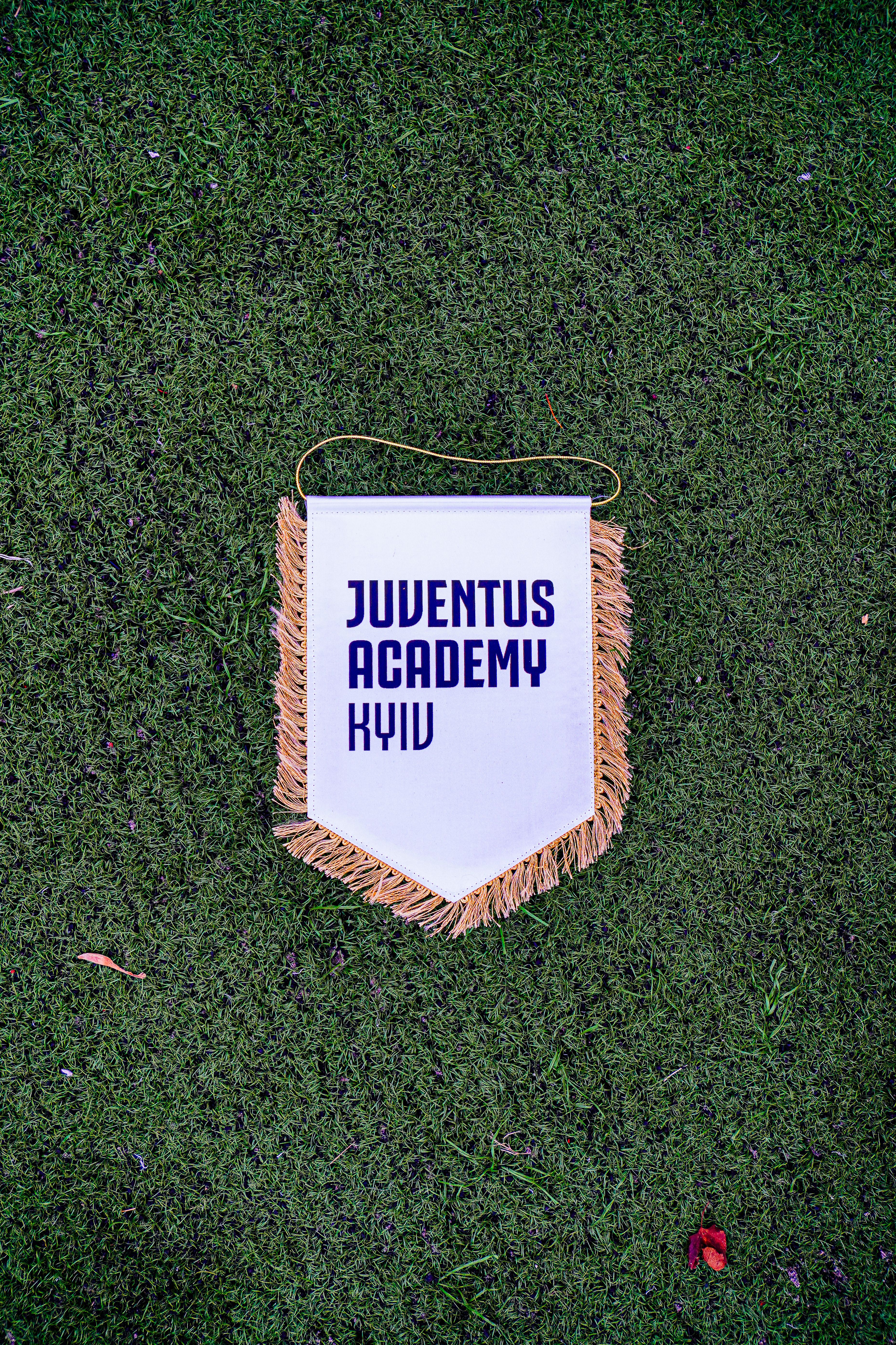 White Juventus Academy Kyiv flag with fringe on green grass field.