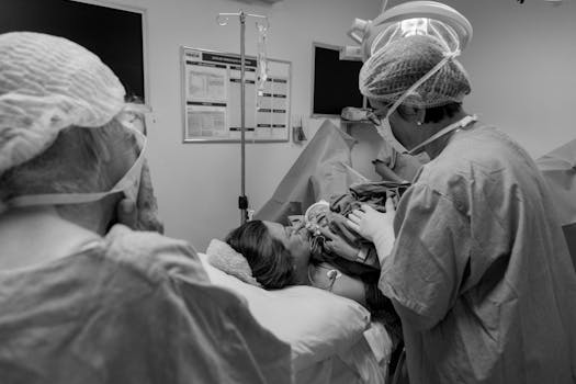 A hospital delivery room scene with doctors and a newborn in black and white.