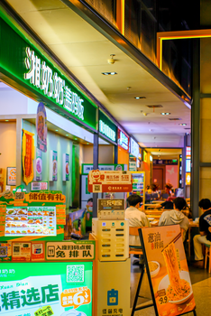 Bustling Asian mall food court with neon signs and patrons dining, creating a lively atmosphere.