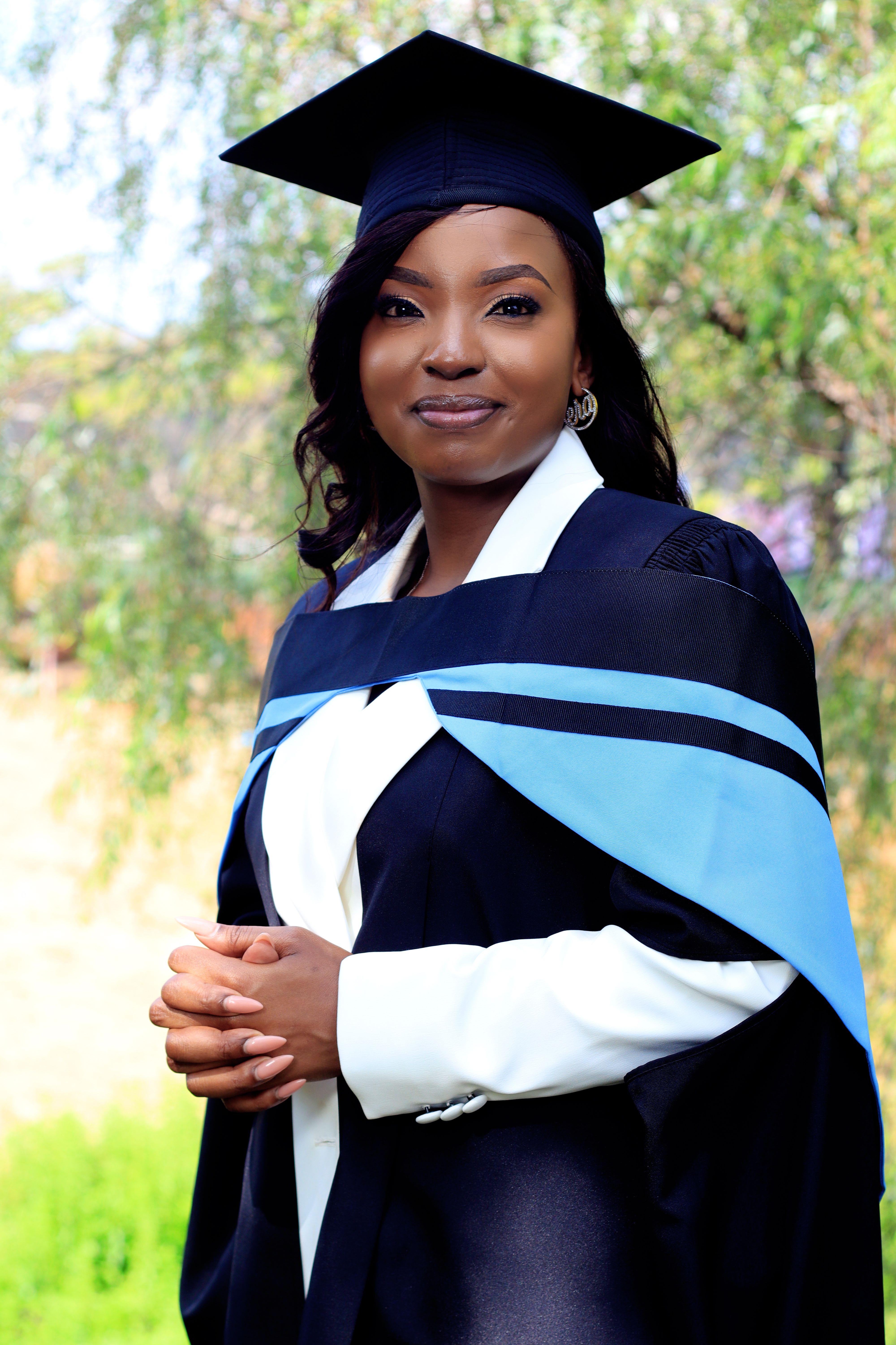 A proud graduate posing outdoors in cap and gown, celebrating her achievement.