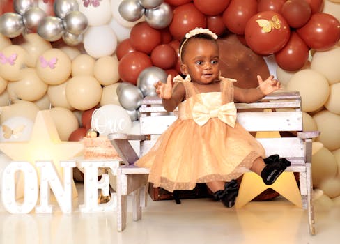 Cute baby girl in festive dress during her first birthday photo shoot with colorful balloons.