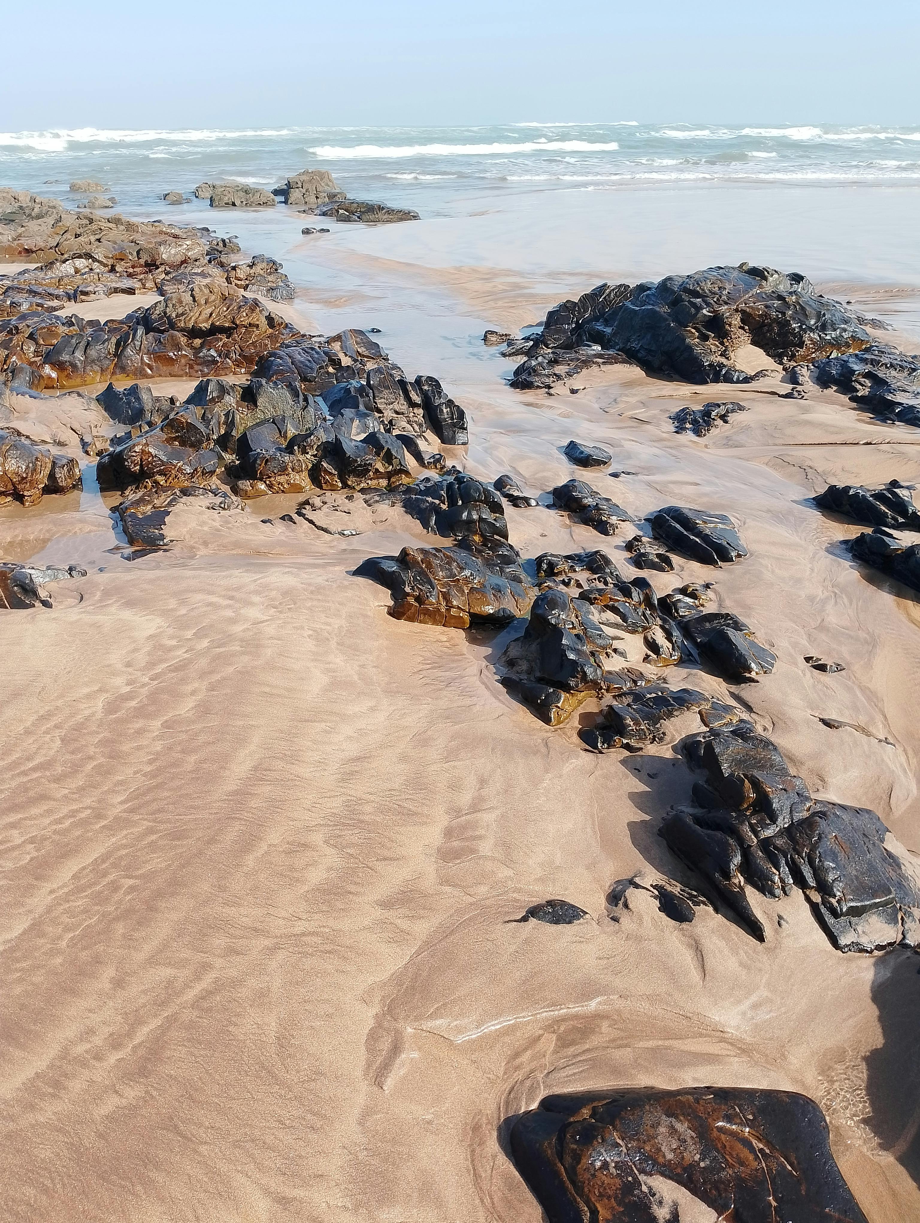 Enchanting beach: golden sands alluring, emerald rocks stunning, tides reveal amazing sandy deposits, waves roll gently, sky azure breathtaking.