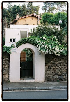 Elegant Mediterranean villa with lush greenery and stone archway on a quiet street.