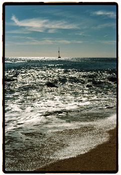 Tranquil beach scene with gentle waves and a distant sailboat against a beautiful sunset.