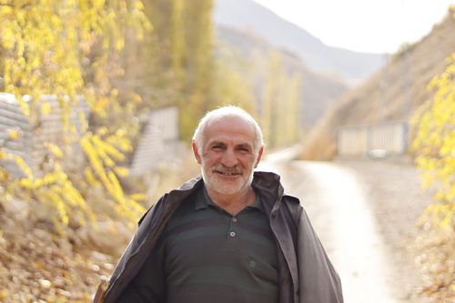 Free Senior man smiling while standing on a sunlit path in a rural mountain area during fall. Stock Photo