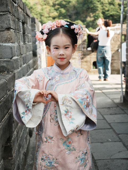Free Young girl wearing traditional Hanfu poses at a historical landmark, making a heart shape with her hands. Stock Photo