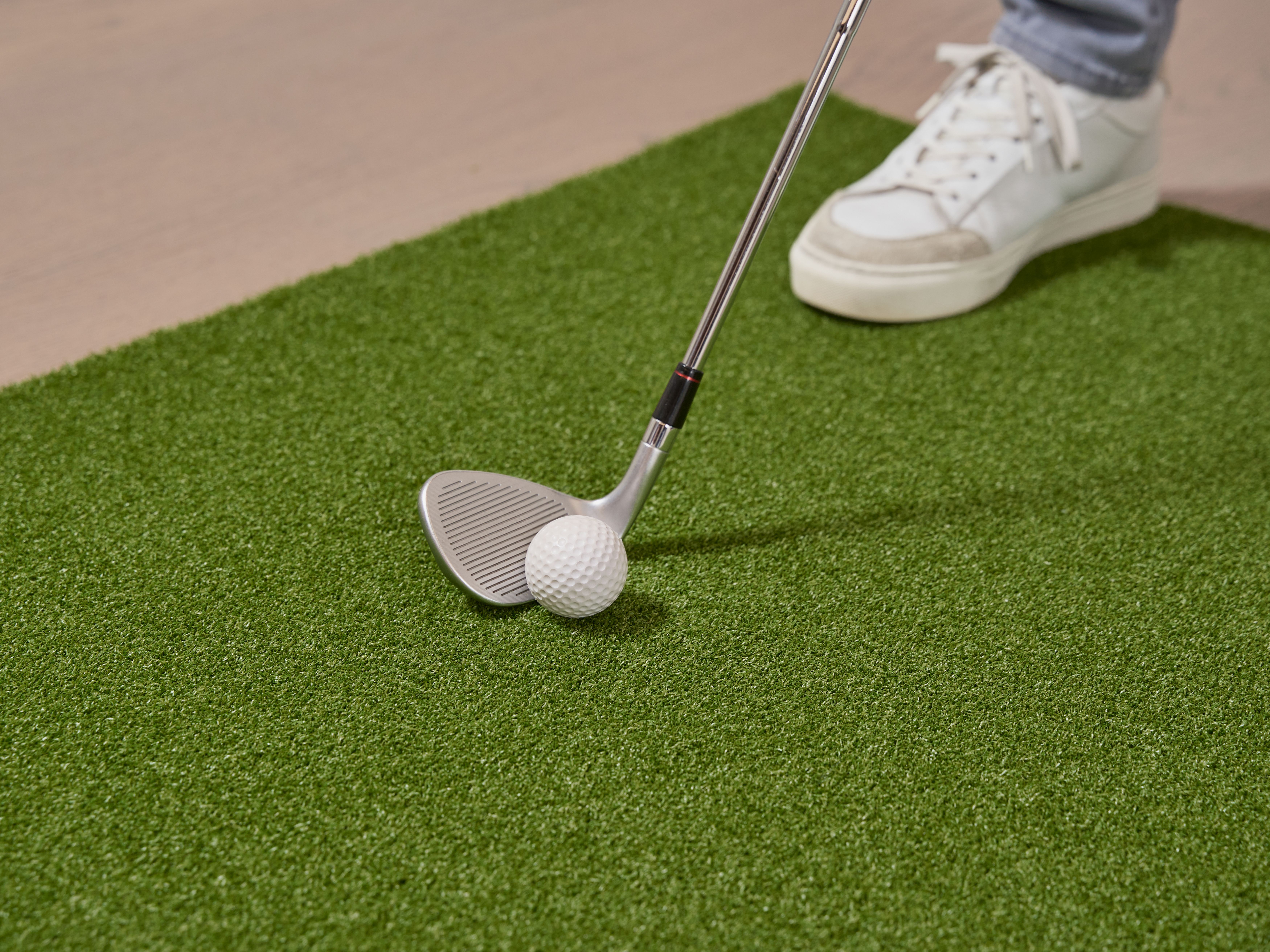 Close-up of a golf club and ball on an artificial putting green indoors.