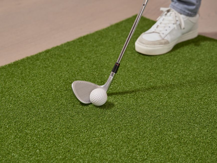 Close-up of a golf club and ball on an artificial putting green indoors.