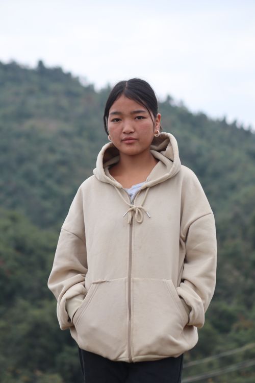 Free Portrait of a young woman in a beige hoodie standing outdoors with hills in the background. Stock Photo