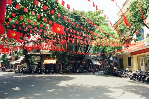 Free A bustling Vietnamese street adorned with red flags and motorbikes, showcasing local culture. Stock Photo