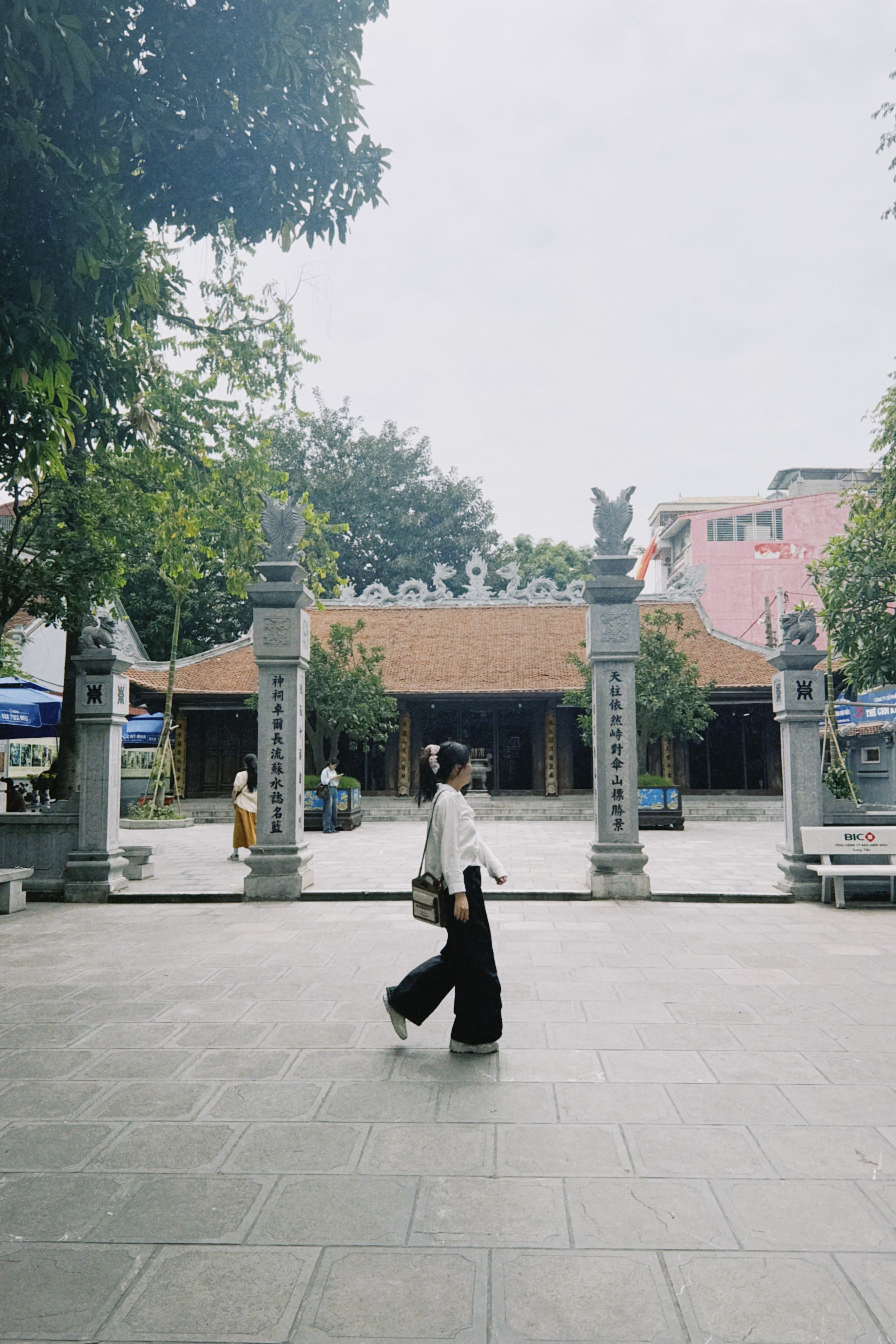A woman walks past a historic temple entrance with towering stone pillars.