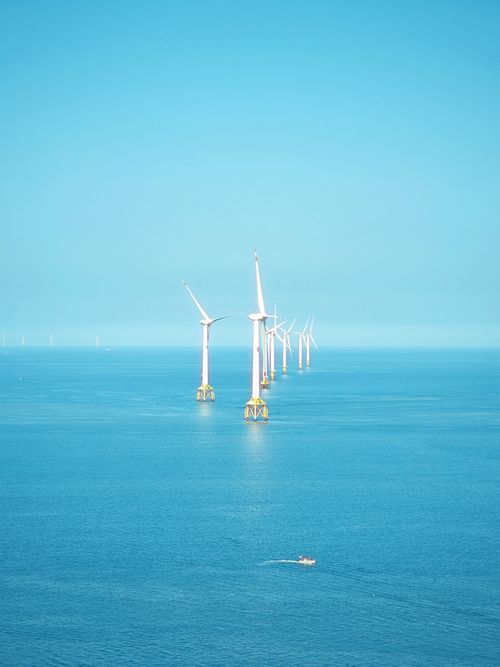 Free A serene view of offshore wind turbines in a calm blue ocean under a clear sky. Stock Photo