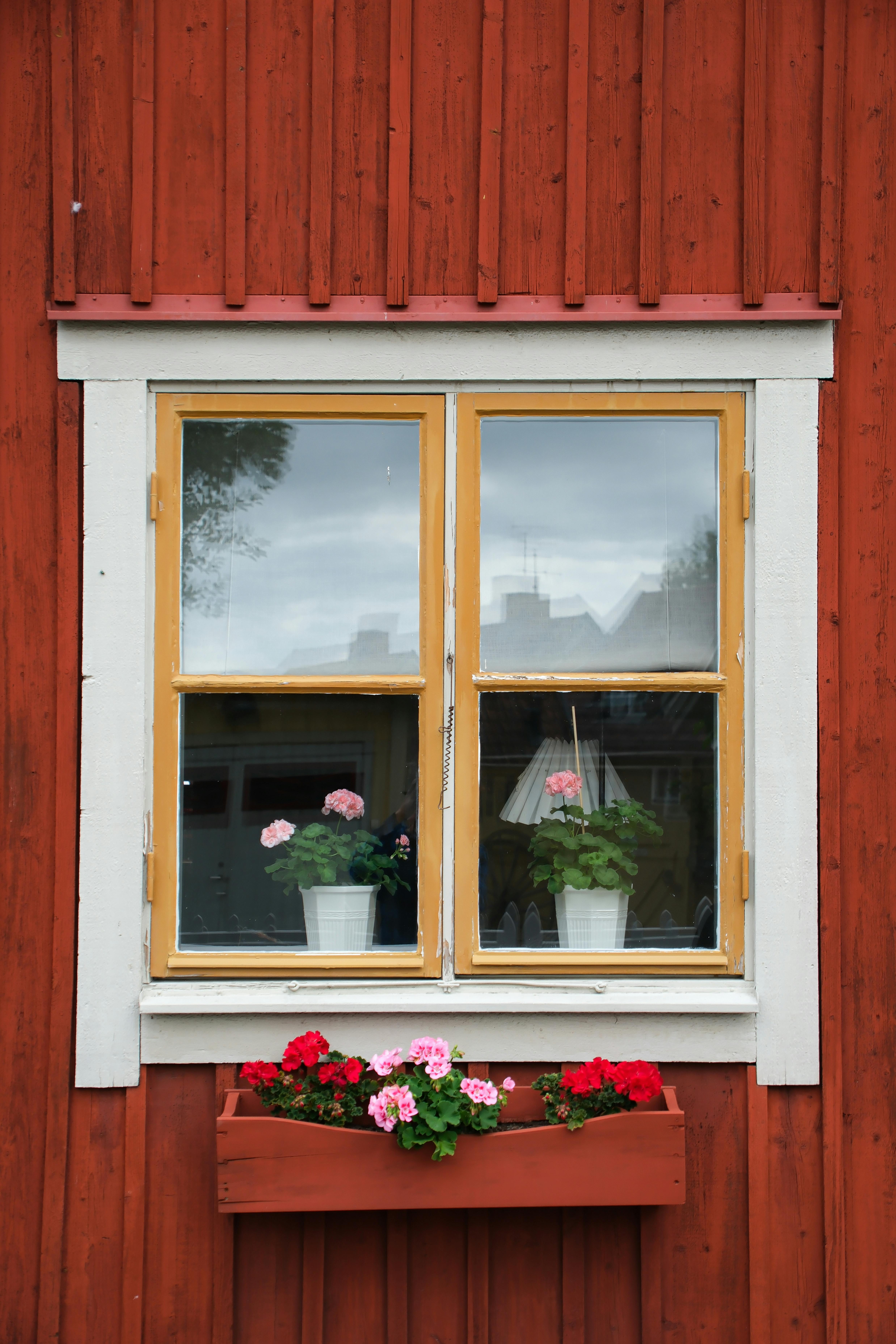 Vintage wooden house facade with charming window and vibrant potted flowers.