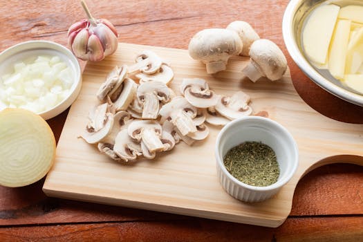 A wooden chopping board with fresh mushrooms, garlic, onion, and herbs ready for cooking.