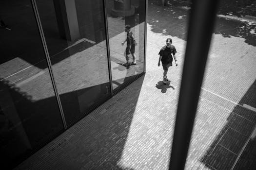 A person walks outdoors reflected in a modern glass facade, creating unique shadows.