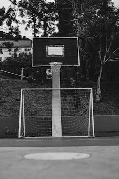 A unique black and white photo of a street basketball hoop above a soccer goal post.