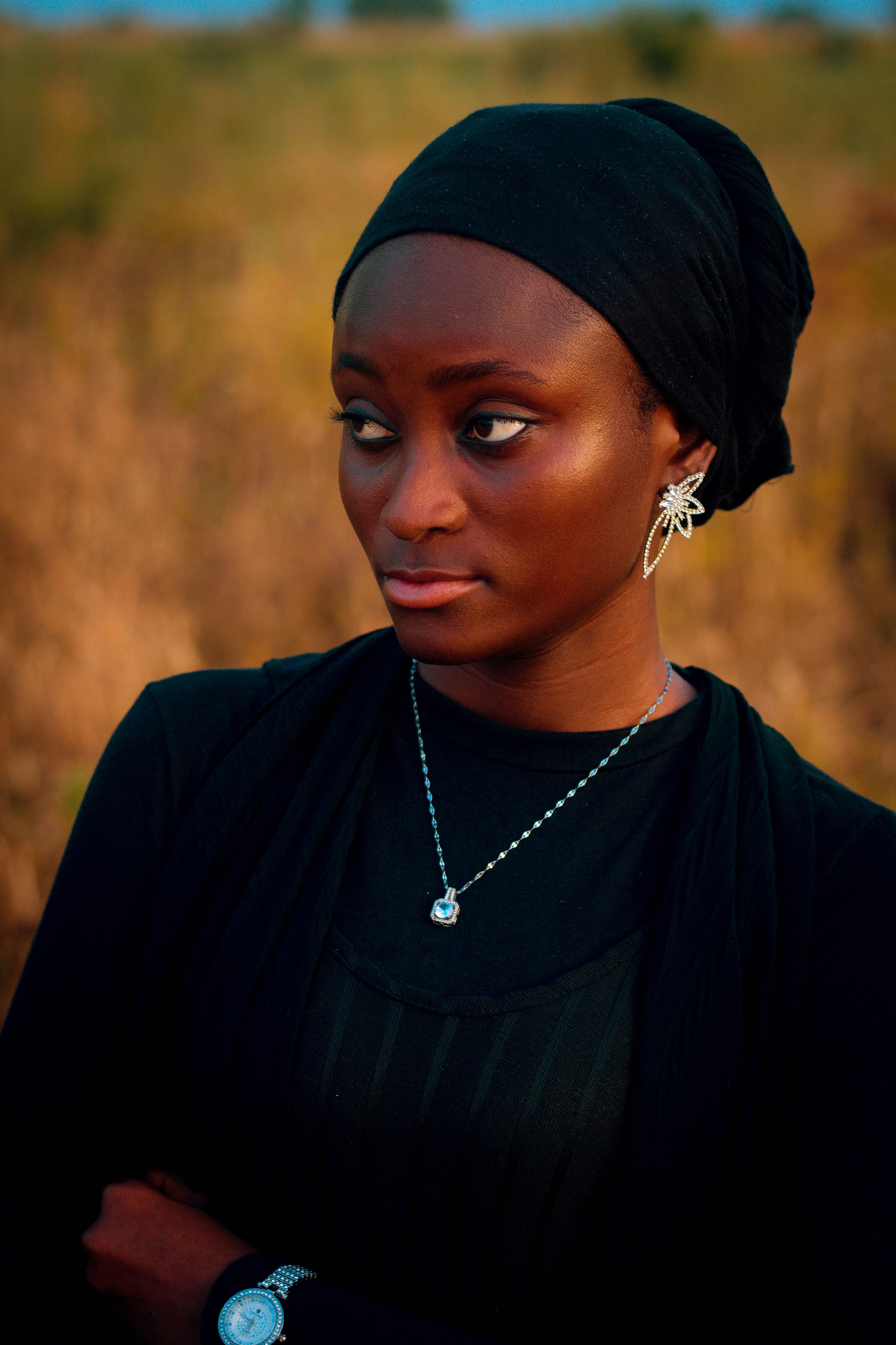 Thoughtful woman in black hijab and jewelry posing outdoors during daytime