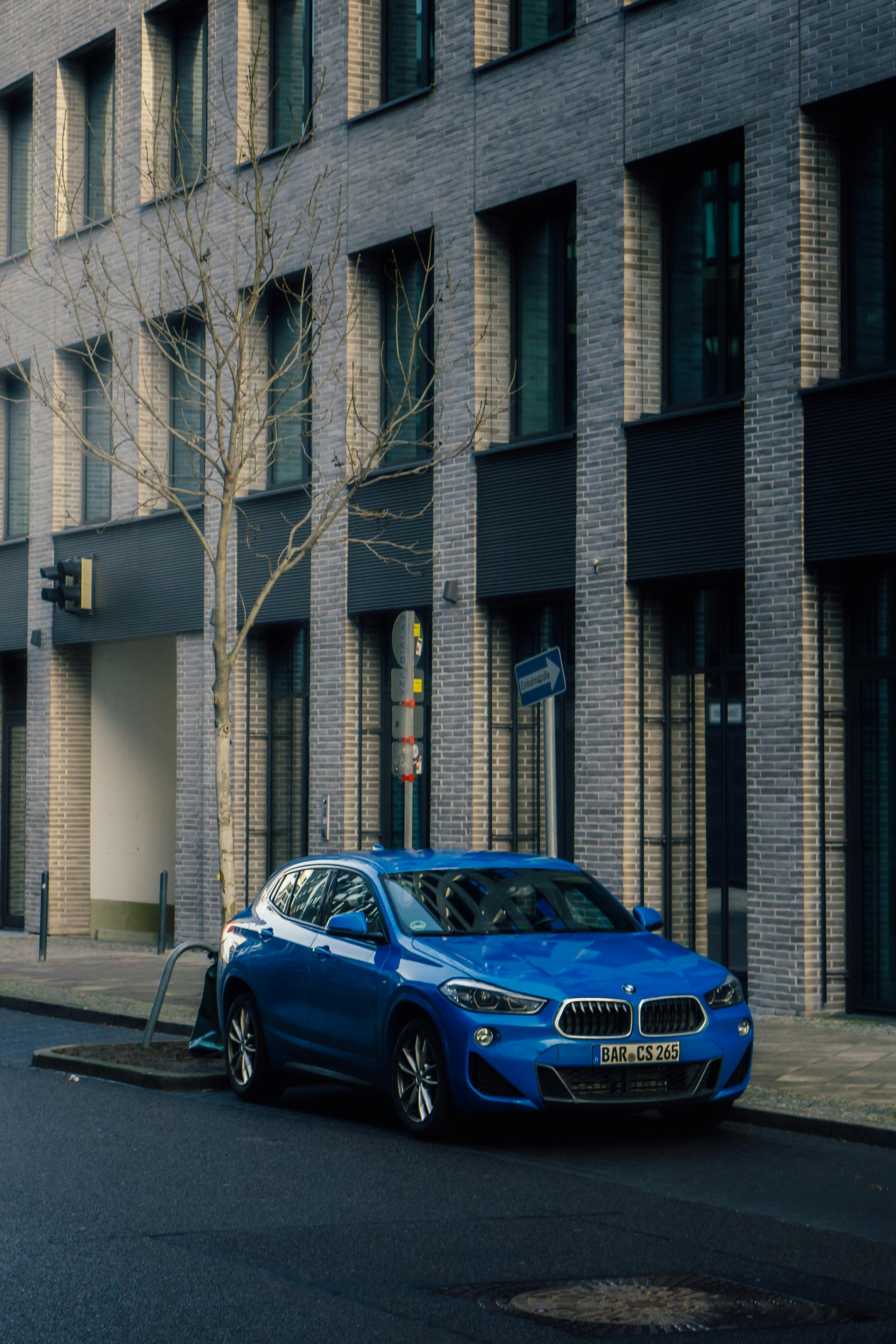 bezplatná Zářivě modré auto zaparkované na městské ulici vedle moderní cihlové budovy ve dne. Základová fotografie