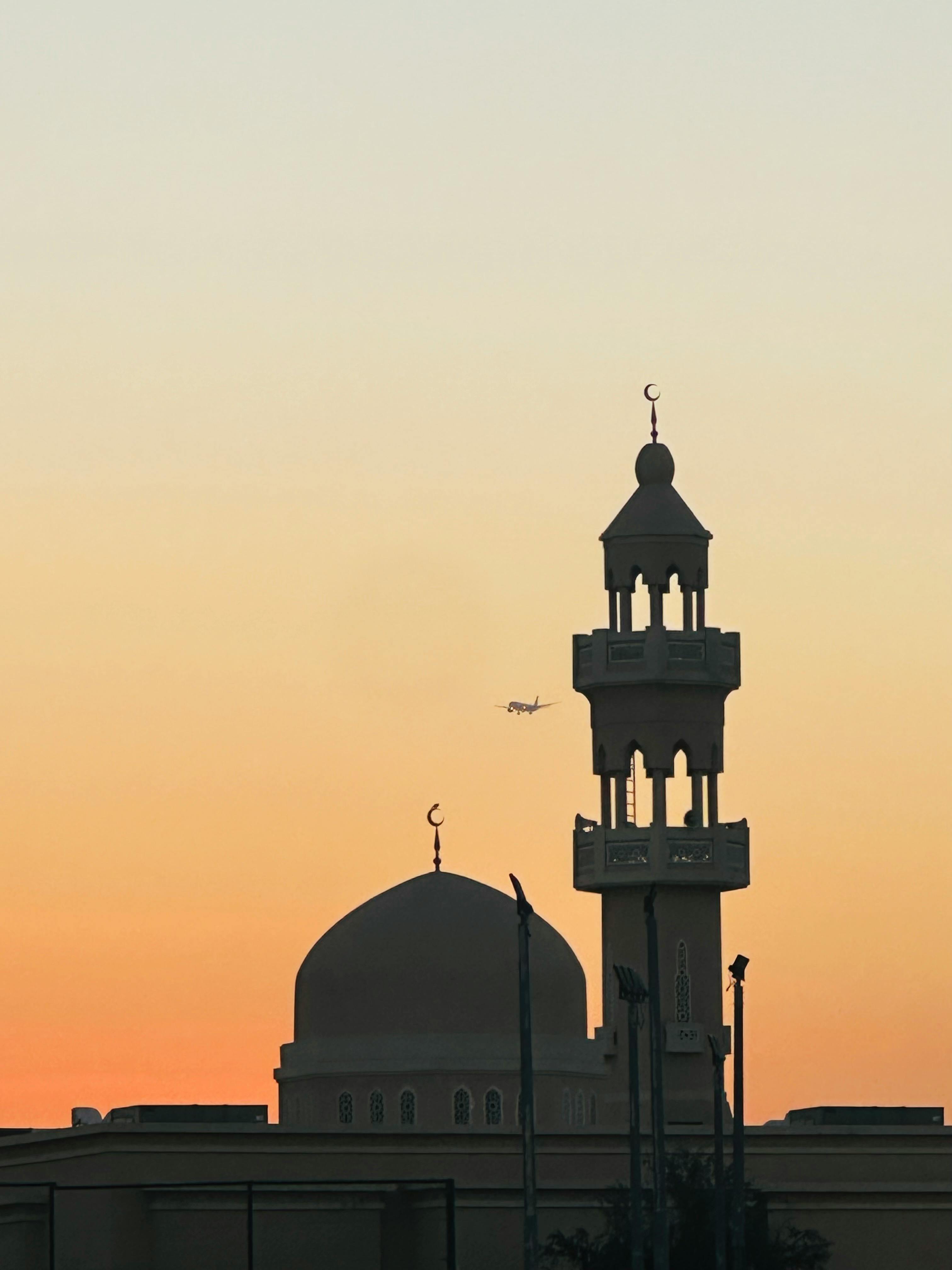 Gratis Silhouette di una moschea contro un vivace cielo al tramonto a Dubai, Emirati Arabi Uniti, con un aereo in vista. Foto a disposizione