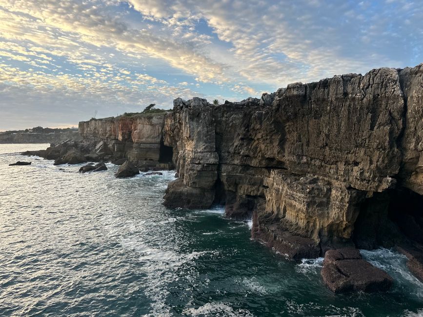 Spectacular view of crashing waves against rugged cliffs in Cascais, Portugal during a beautiful sunset.
