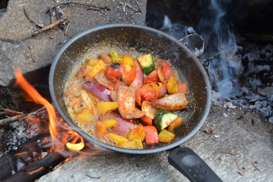 A vibrant assortment of vegetables sizzling in a skillet over a campfire, perfect for outdoor cooking inspiration.