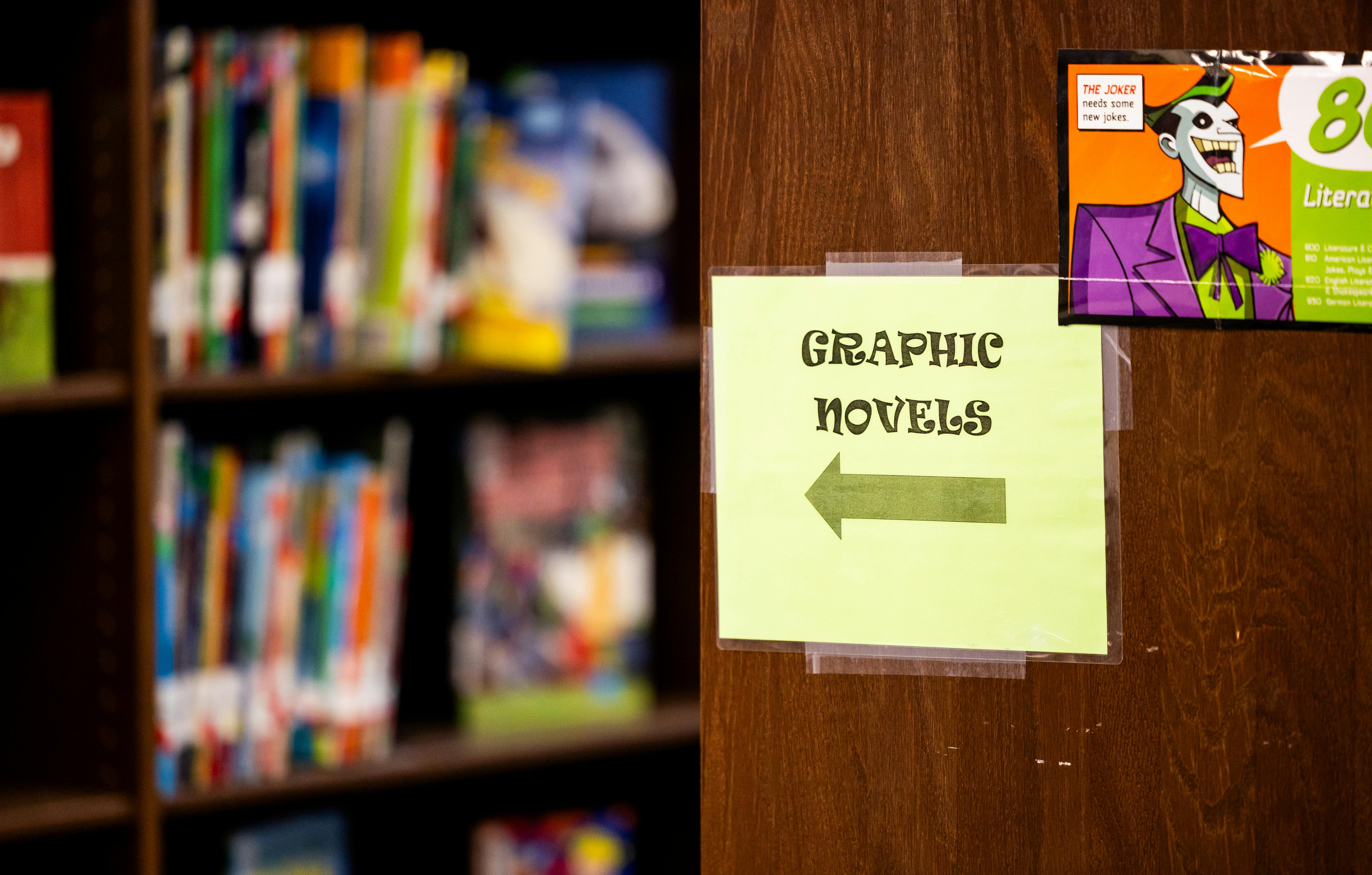Graphic novel section sign in a library with shelves of colorful books in the background.
