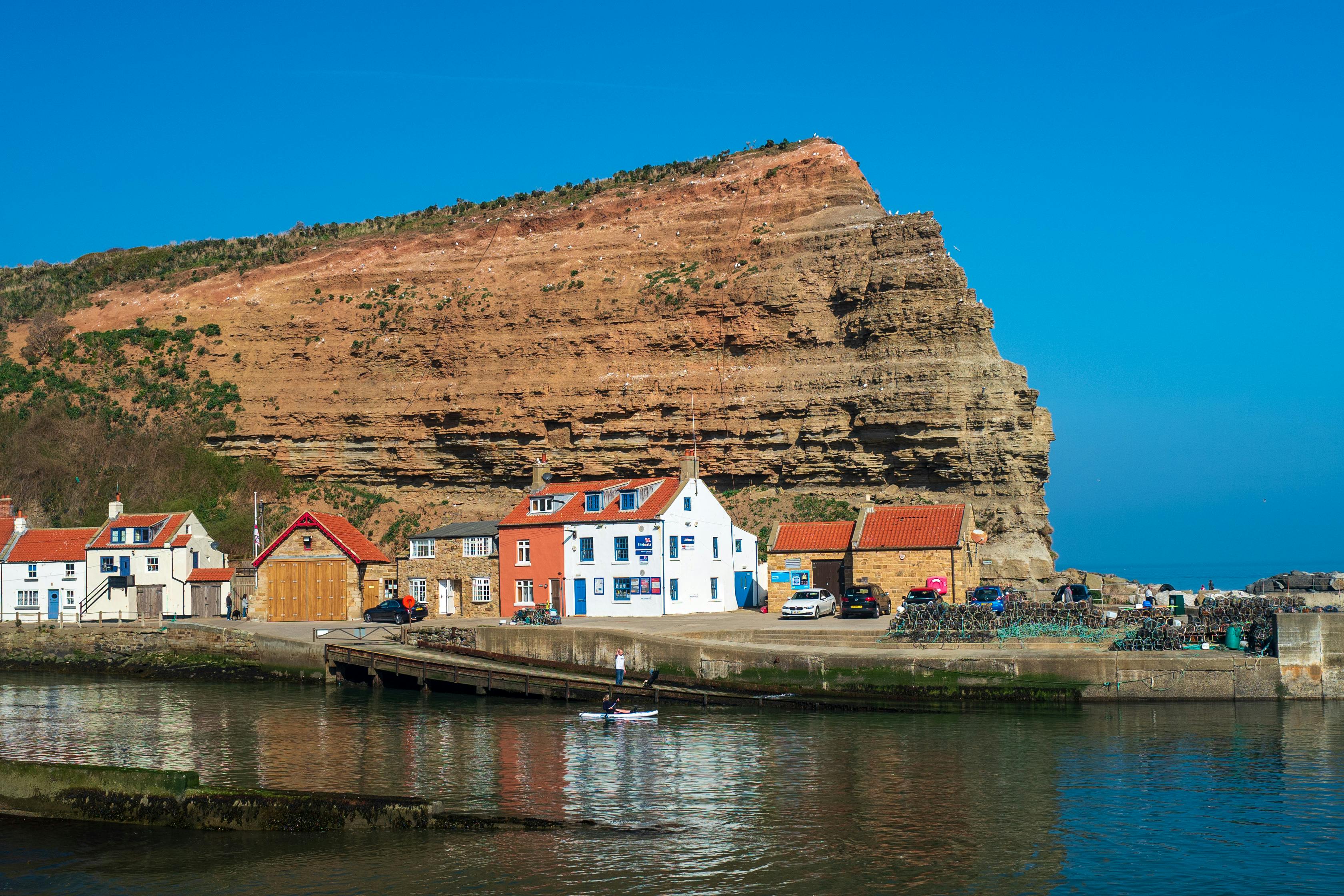 Cliffs in Staithes with picturesque harbor, boats, and quaint houses under a bright blue sky.
