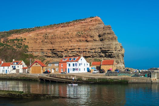 Cliffs in Staithes with picturesque harbor, boats, and quaint houses under a bright blue sky.