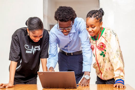 Three young adults collaborating on a laptop for a digital project indoors.