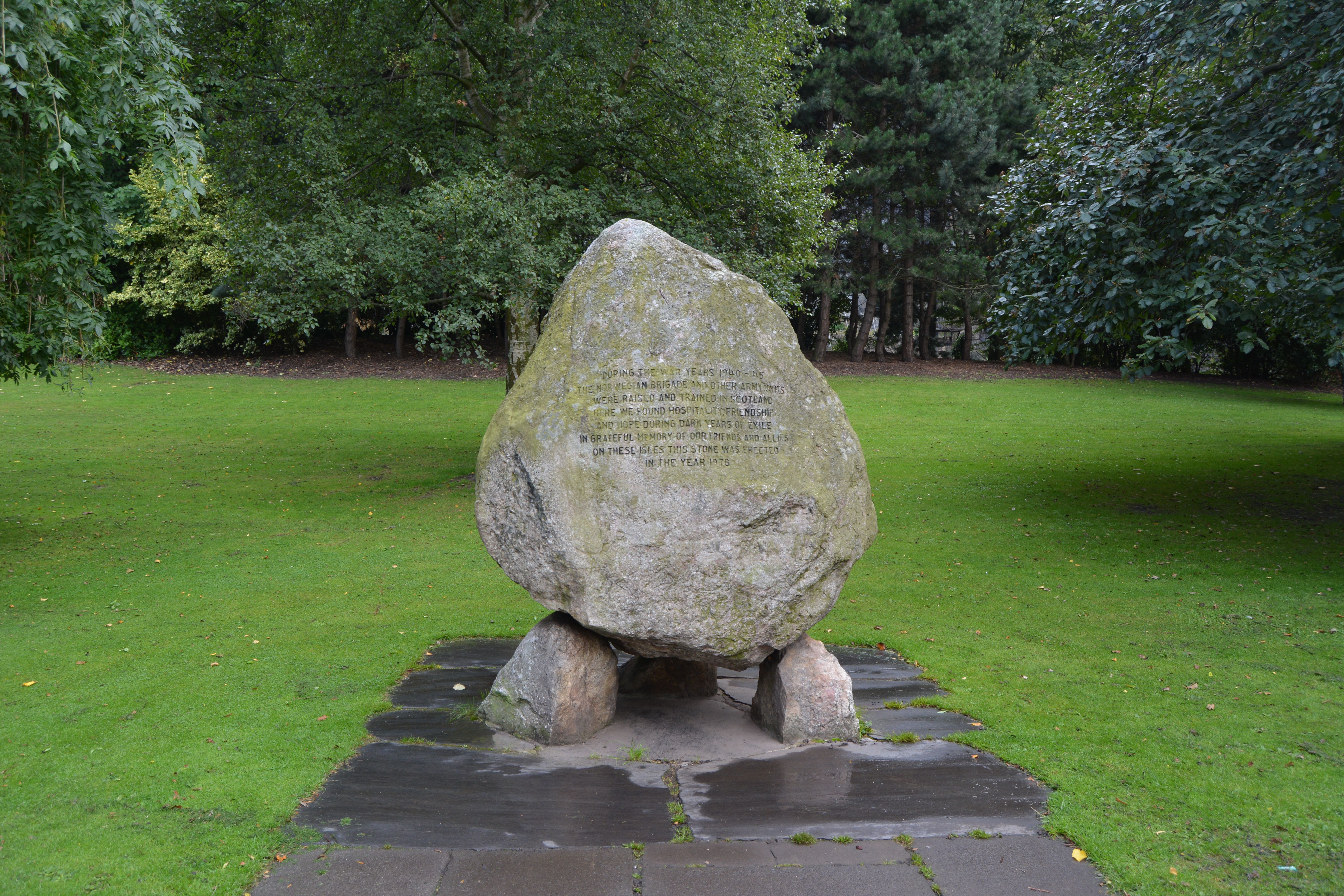 A large stone monument set in a green park in Scotland, surrounded by lush trees.