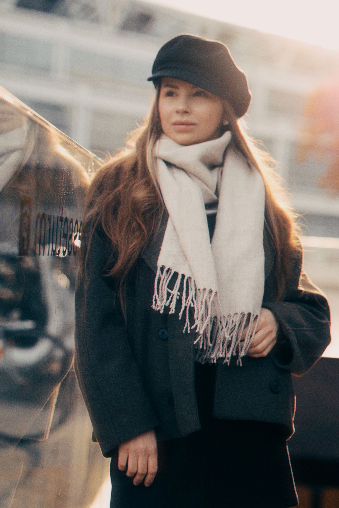 Woman in a black coat, cream scarf, and newsboy cap